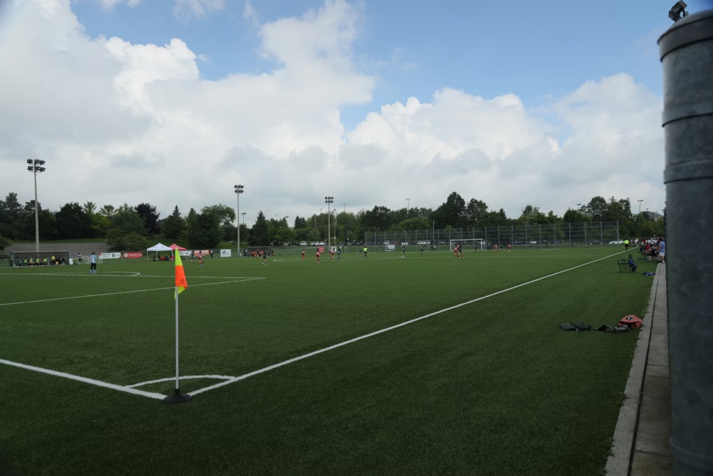 Campo de futebol, focado na linha de fundo e no escanteio, com bandeira amarela e laranja em destaque